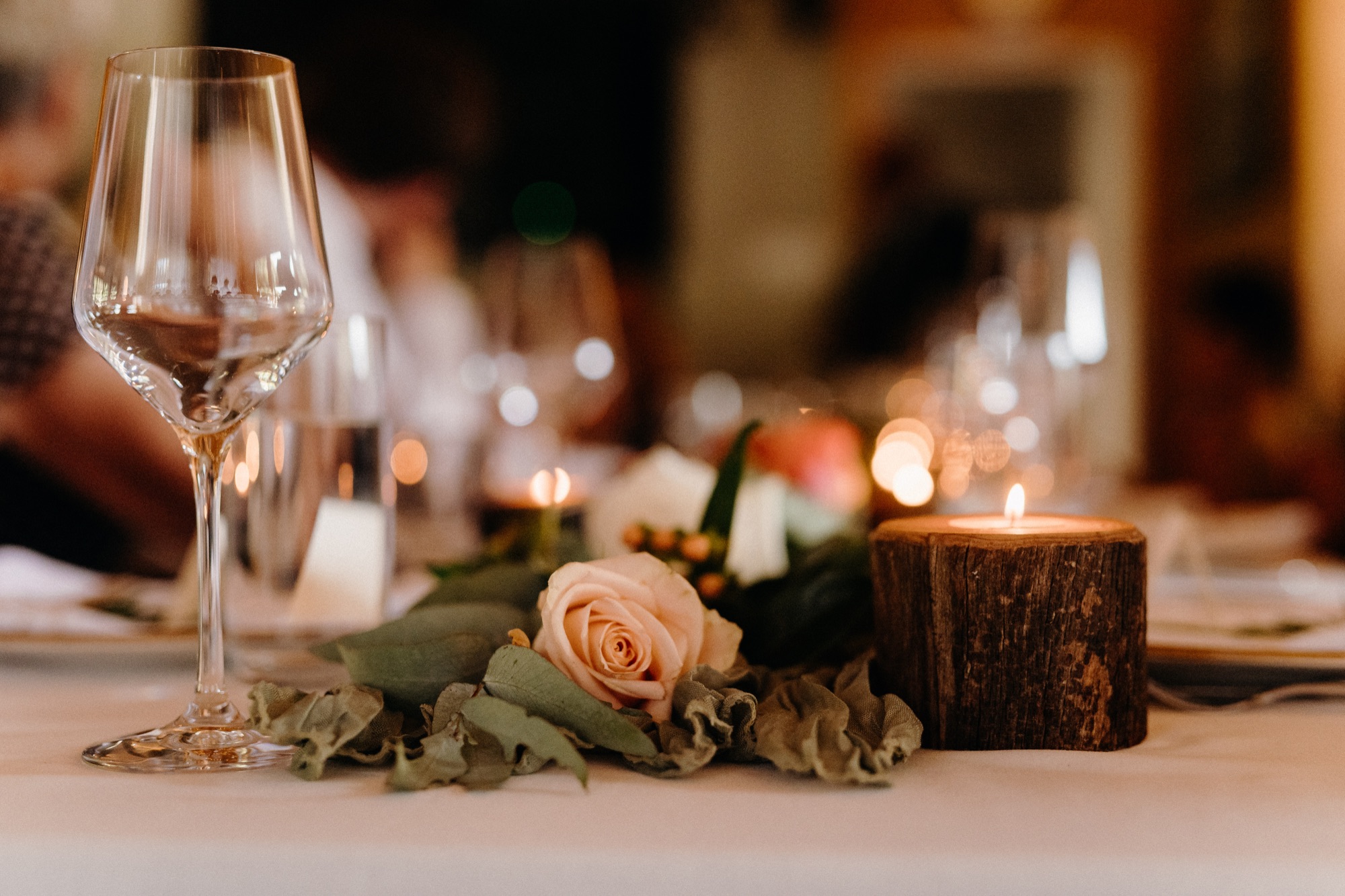 A wine glass, rose and candle on a wooden block at a styled reception table